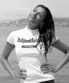 a woman with her hands on her hips posing for a photo by the water in black and white