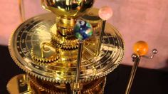 a gold clock with gears and glass balls on it's sides, sitting on a table