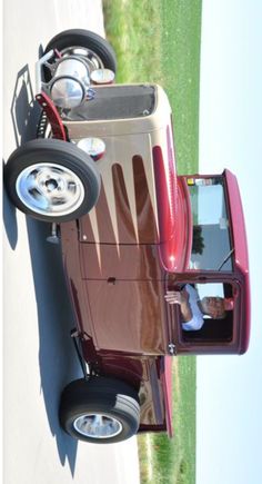 an old model car is parked on the side of the road in front of some grass