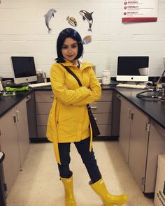 a woman wearing yellow rain boots standing in a kitchen with her arms crossed and looking at the camera