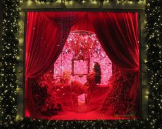 a woman sitting in front of a window with red curtains and lights on it's windowsill