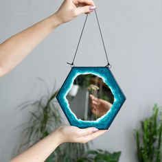 a person holding up a mirror hanging from a string in front of a potted plant