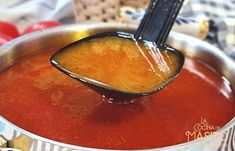 a ladle full of tomato sauce being held by a wooden spoon