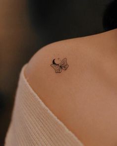 a small butterfly tattoo on the back of a woman's shoulder