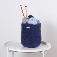 a blue felt basket with yarn and knitting needles in it sitting on a white table