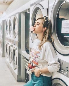 a woman sitting on the side of a washer next to a dryer with her tongue hanging out