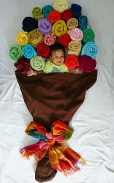 a baby is laying in a large bouquet of colorful yarns on a white sheet