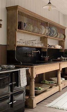 an old fashioned kitchen with black counters and wooden shelves, plates on the shelf above the stove