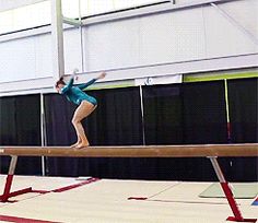 a woman on a balance beam in an indoor gymnastics court with one arm extended and the other leg bent