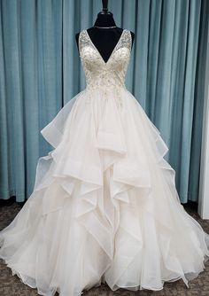 a wedding dress is displayed on a mannequin in front of a blue curtain