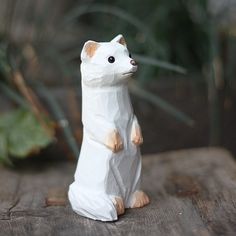 a white cat figurine sitting on top of a wooden table next to a plant