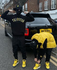 two people in black and yellow outfits standing next to a car