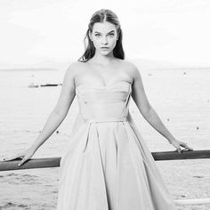 a woman in a pink dress standing on a pier next to the ocean with her hands on her hips