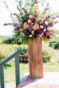 a tall wooden vase filled with lots of flowers on top of a table next to a stair case