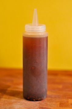 a bottle filled with liquid sitting on top of a wooden table next to a yellow wall