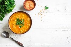 a bowl of soup next to two spoons and parsley