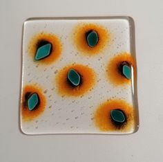 a square glass plate with orange and green decorations on it's edges, sitting on a white surface