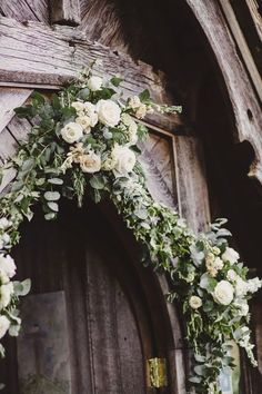 a wedding arch with white flowers and greenery hanging from it's front door