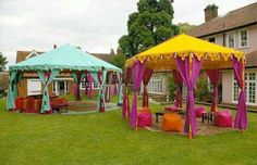 two colorful tents sitting on top of a lush green field next to a house and lawn