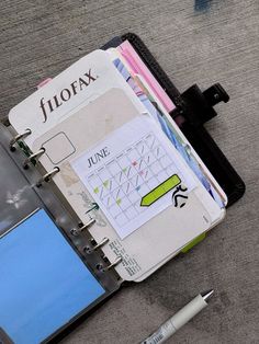 an open planner book sitting on the ground next to a pen