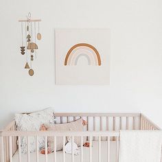 a baby crib in a white nursery with a rainbow print on the wall and hanging decorations