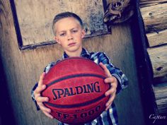 a young boy holding a basketball in front of a wooden door with the word spalding on it