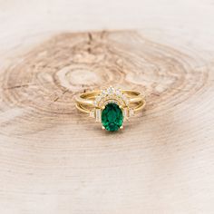 an emerald and diamond ring sitting on top of a piece of wood