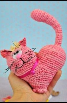 a pink crocheted cat with a flower on its head is held up in front of a blue background