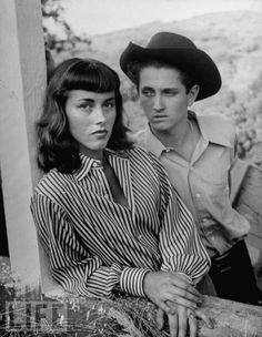 black and white photo of man and woman leaning against wall with mountains in the background