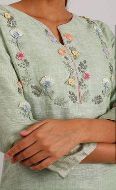 a woman wearing a green dress with floral embroidery on the chest and sleeves, holding her hands together