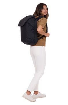 a woman in white pants is carrying a black backpack