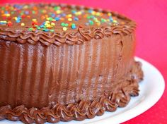 a chocolate frosted cake with sprinkles on a white plate against a red background