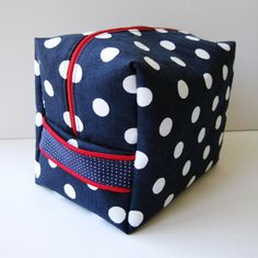 a blue and white polka dot bag with red zippers on the front, sitting on a table