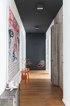 an empty hallway with wooden floors and artwork on the wall, along with two chairs