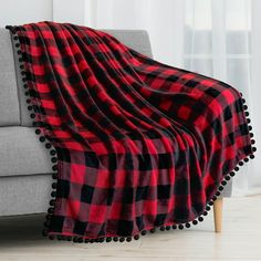 a red and black plaid blanket with pom - poms on the edge next to a couch