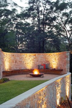 an outdoor seating area with lights on the wall and grass in the foreground, surrounded by trees