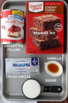 ingredients to make brownie mix in a baking pan on a wooden counter top, including cream cheese, sugar and cherry fudge