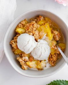 a bowl filled with fruit and ice cream on top of a white table next to pink flowers