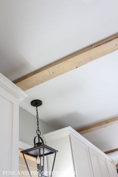 a light fixture hanging from the ceiling in a kitchen with white cabinets and wood beams