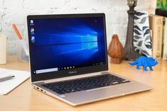 an open laptop computer sitting on top of a wooden desk next to a blue dinosaur figurine