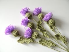 small crocheted flowers are arranged on a white surface with green stems and purple petals