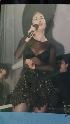 a woman in a black dress holding a microphone and singing into a microphone while standing next to a man