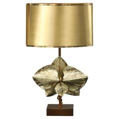 a table lamp with a gold shade on the base and a flower shaped glass decoration