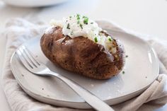 a white plate topped with a baked potato covered in cottage cheese and chives next to a fork