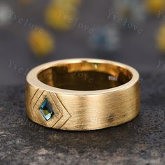 a gold wedding band with a blue diamond in the center on top of a granite surface