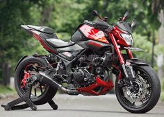 a red and black motorcycle is parked on the side of the road in front of some trees