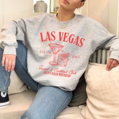 a woman sitting on top of a couch wearing a sweatshirt with las vegas written on it