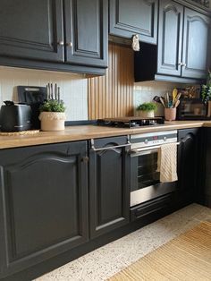 a kitchen with black cabinets and wooden counter tops is pictured in this image, there are potted plants on the stove