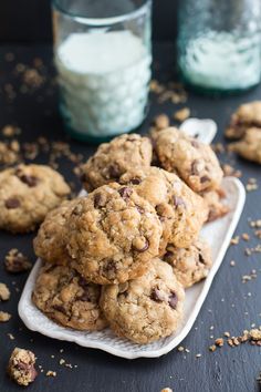 chocolate chip cookies on a white plate with crumbs scattered around them and one cookie in the middle