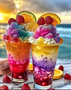 two glasses filled with ice cream and fruit on top of a table next to the ocean